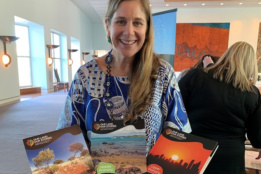 A smiling woman holding up colourful books