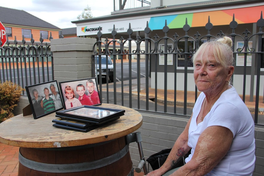 A woman sits at a table with framed photographs of a young children and teens.