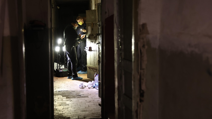 Men with lights search a dark building.