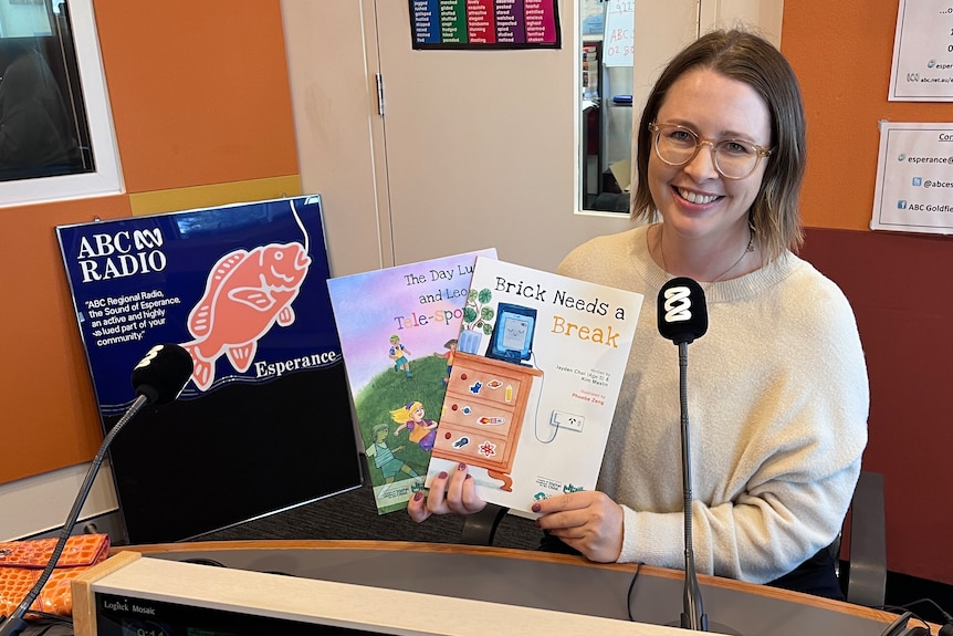A smiling, dark-haired woman holds up two children's books as she sits in a radio studio.