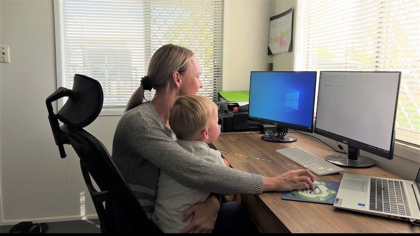 a woman sits at a desk with her son on her lap