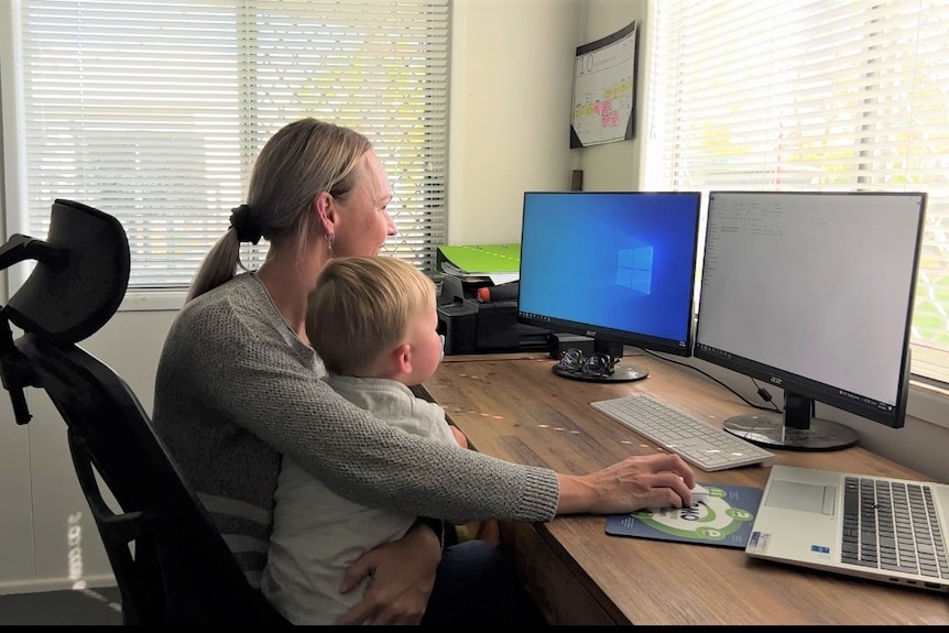 a woman sits at a desk with her son on her lap