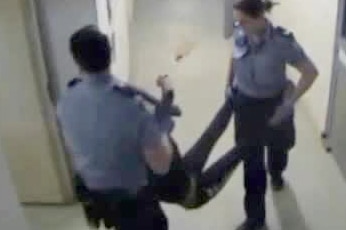 Ms Dhu is carried by two police oficers by her arms and legs in a corridor.