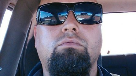 A tight head shot of Jason Craig Headland wearing sunglasses sitting in a car looking at the camera.
