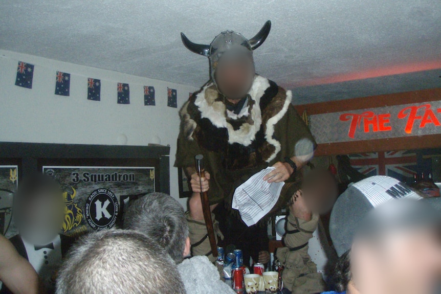 A man dressed as a viking stands on a table with a crowd of men around him.