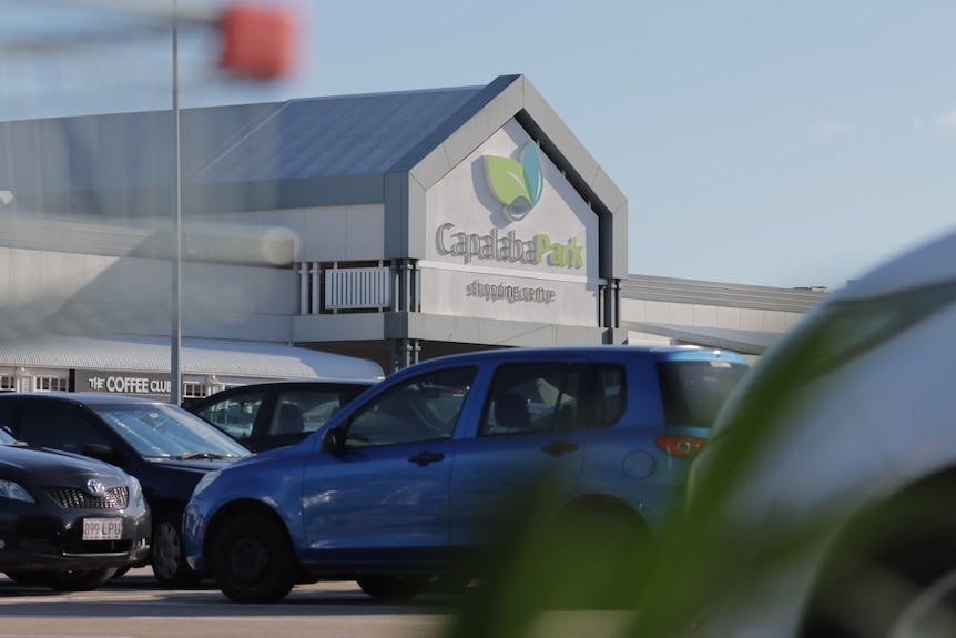 A view of cars in the carpark with a shopping centre behind.