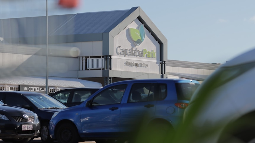 A view of cars in the carpark with a shopping centre behind.