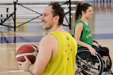 A young man holds a ball and smiles. He is in a wheelchair.