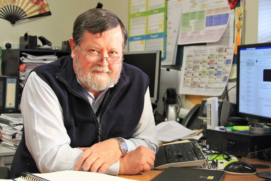 An academic sits at a desk in his office.