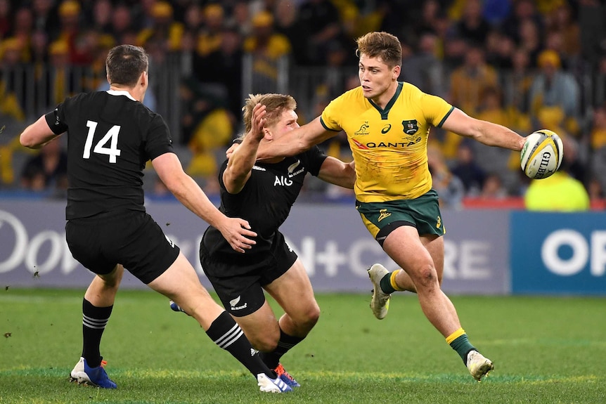 A Wallabies player pushes past an All Black preparing to pass the ball.