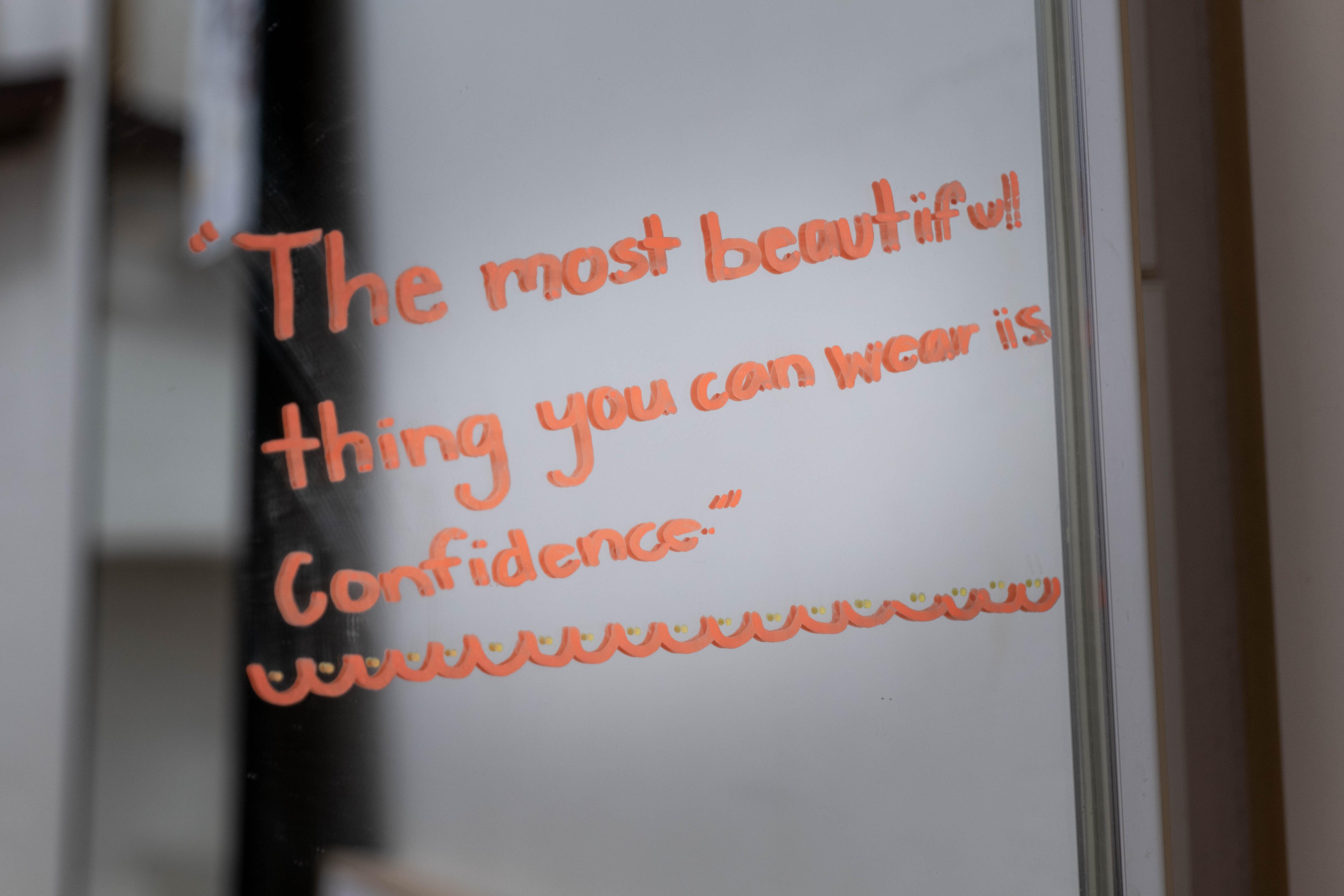 Child-like writing on a mirror in orange saying "The most beautiful thing you can wear is confidence".