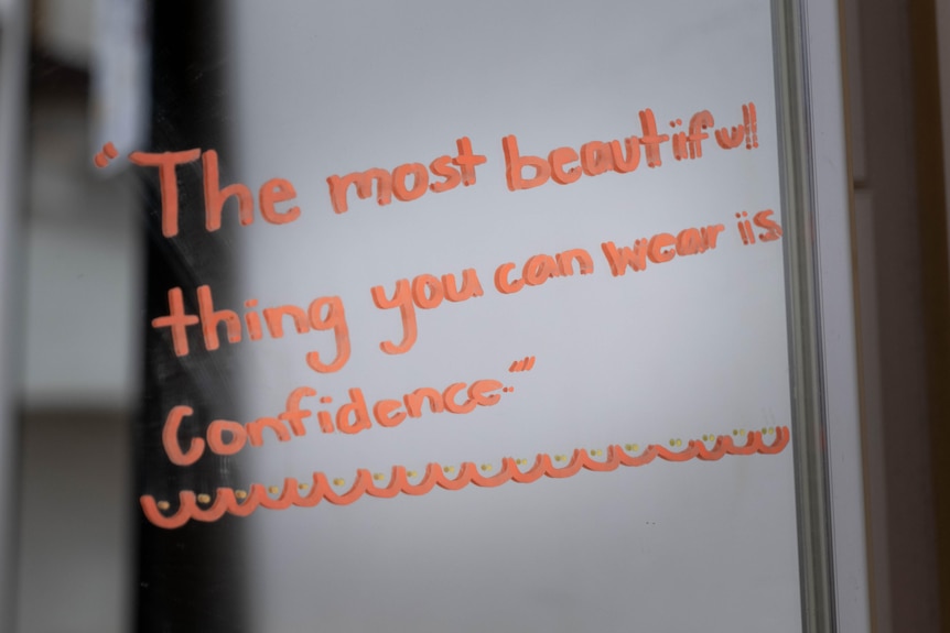 Child-like writing on a mirror in orange saying "The most beautiful thing you can wear is confidence".