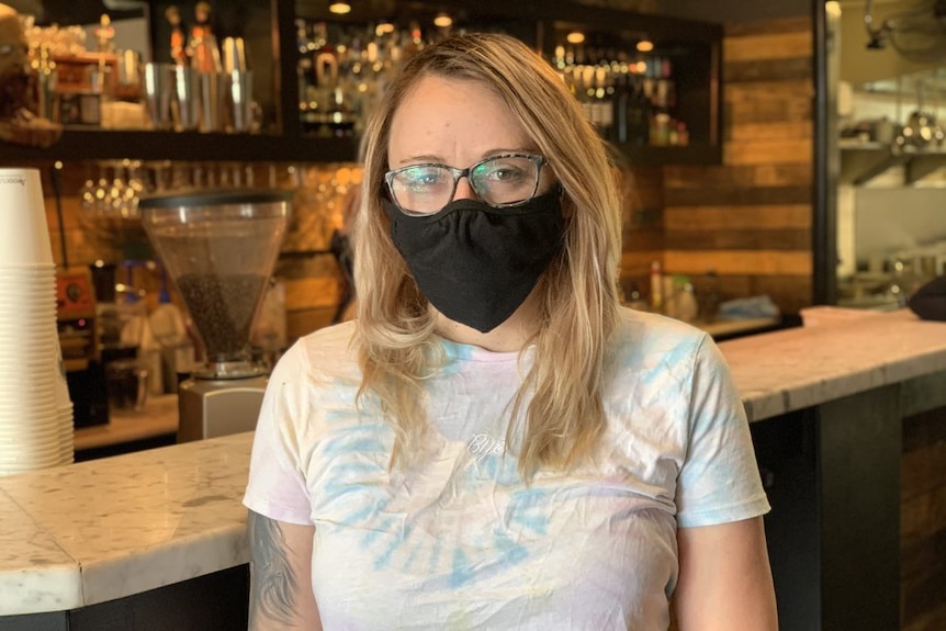 Alicia MacKinnon, wearing a mask, stands inside her bar.