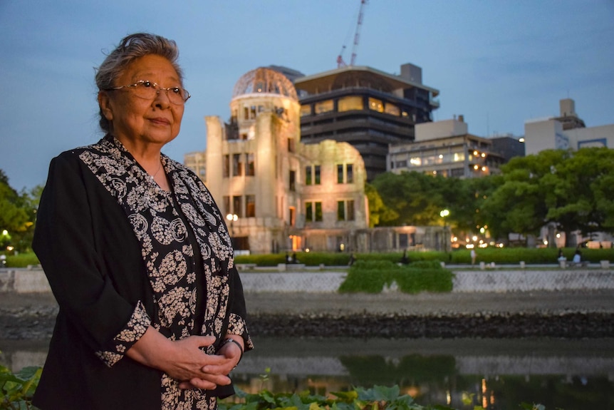 A women stands in front of the construction of a dome building by a river.