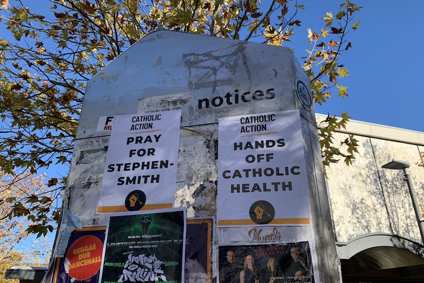 Posters on a concrete noticeboard that read "Pray for Stephen-Smith" and "Hands of Catholic health".