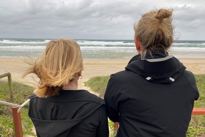Two women staring at rough seas from the beach.