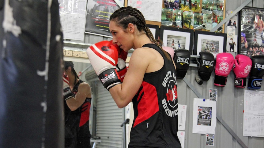 Young woman with her hair in tight plates boxing a large black boxing bag