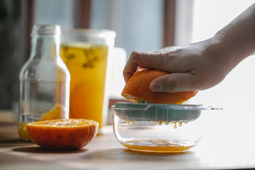 An orange being juiced by hand for analysis of how healthy fruit juices are.