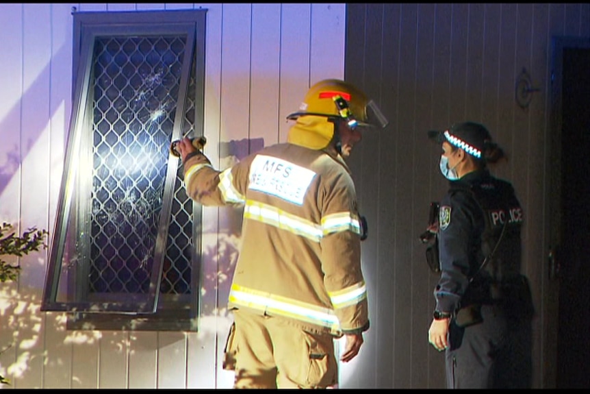 An MFS officer speaks to a police officer as they shine a torch through the window of a house