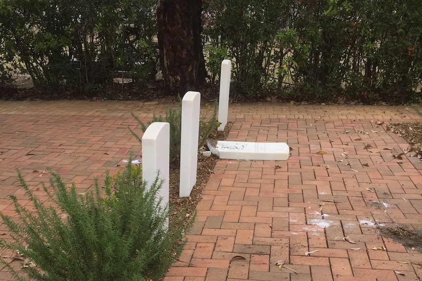 A side-on shot of four headstones. One of them lies flat on the ground, having been knocked over.