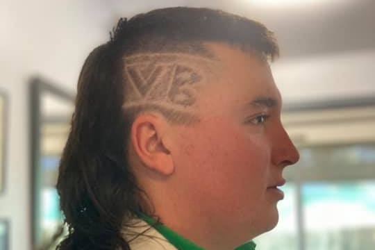 A boy has 'VB' shaved into the side of his head, showing off a long mullet. 
