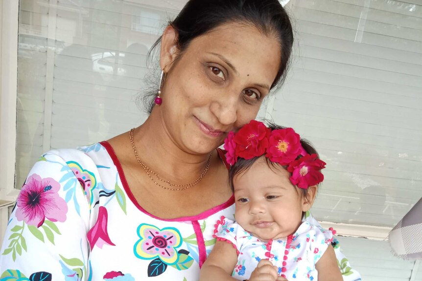 A woman smiles with her head tilted as she holds a baby girl wearing a flower headband