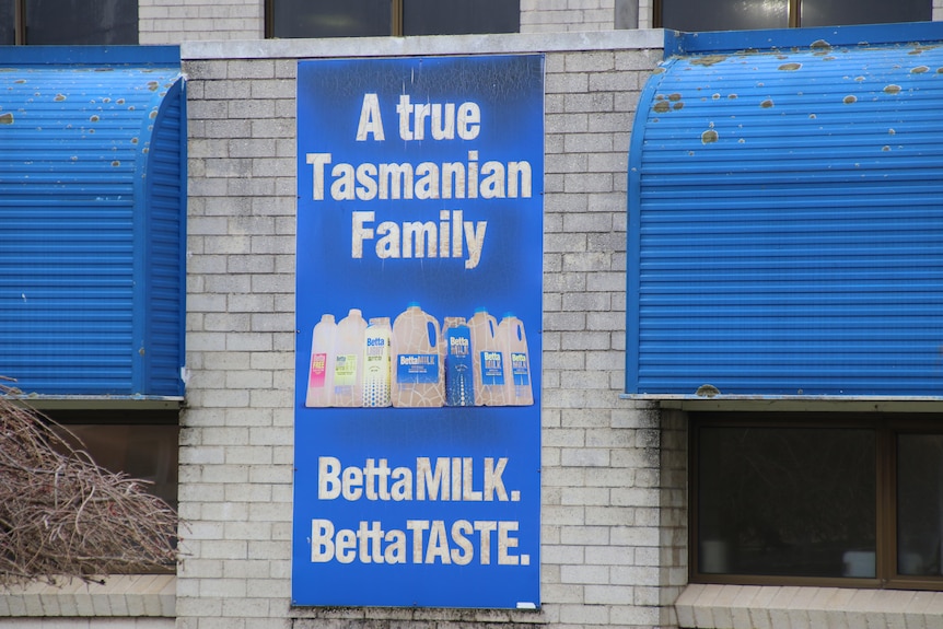 A bright but dirty blue sign for Better Milk adorns a grey, daggy factory wall.