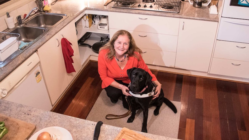 Woman crouches down beside a black dog in her kitchen.