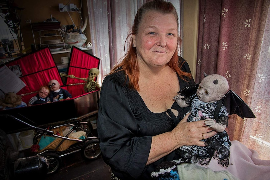 A woman holds a life-sized baby doll painted grey