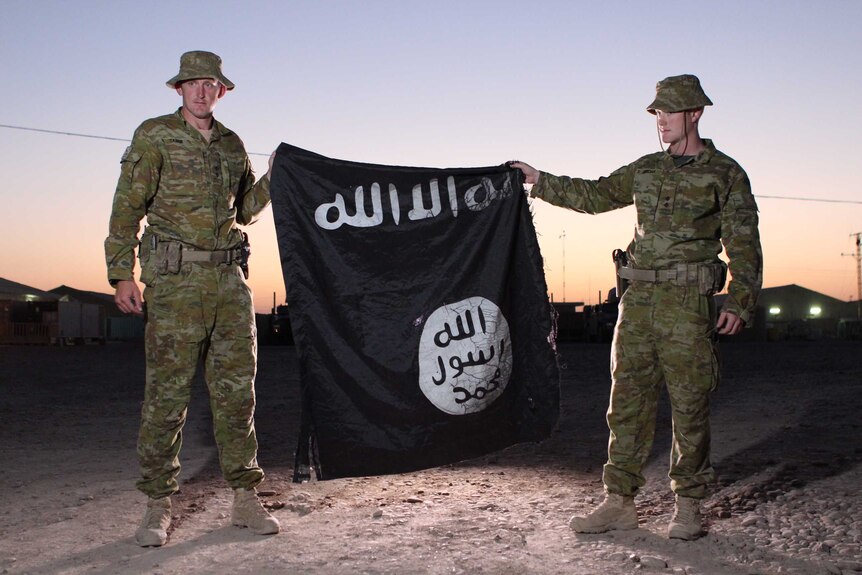 Two Australian soldiers hold a tattered Islamic State flag.