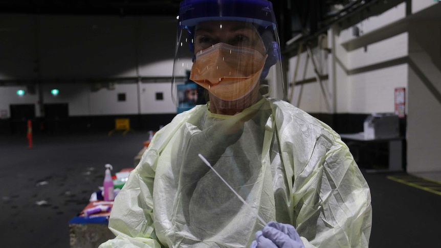 Cheryl wears personal protective equipment and holds a swab.