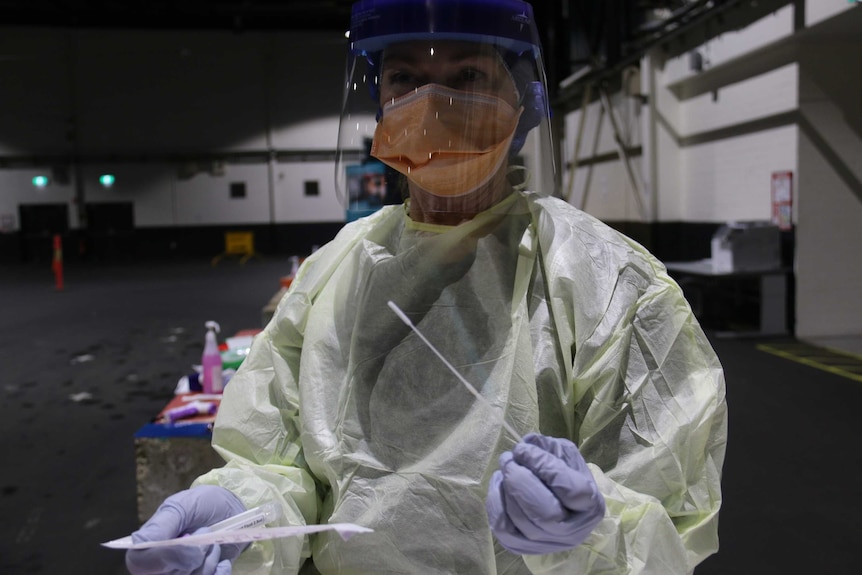 Cheryl wears personal protective equipment and holds a swab.