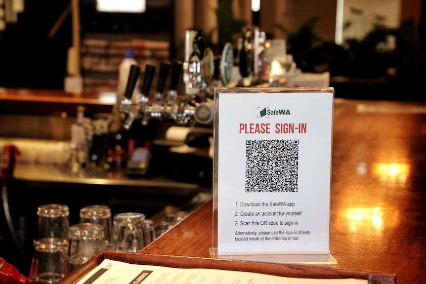 A sign saying 'please sign in' with a QR code on it on a bar.