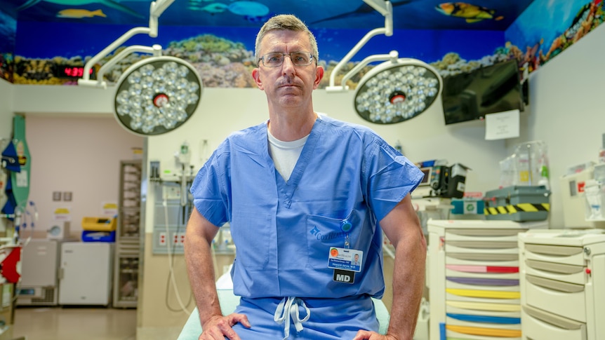 Un uomo con gli occhiali e uno scrub blu siede sul tavolo operatorio in un ospedale 