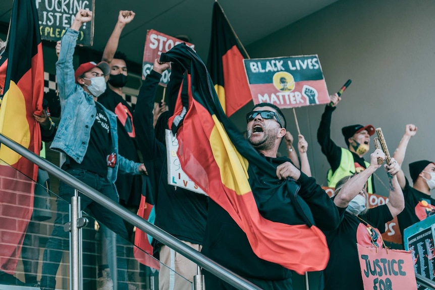 people raise their fists and hold up signs while standing on steps