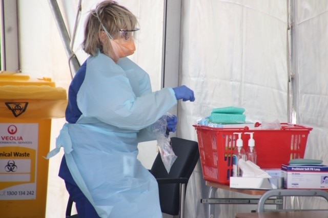 A woman wearing a mask and PPE, surrounded by hand sanitiser and gloves at a Burnie coronavirus testing clinic, Burnie Tasmania.