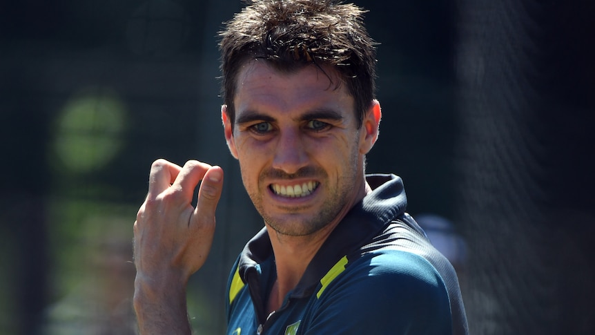 Pat Cummins grimaces with his hand near his face while at training