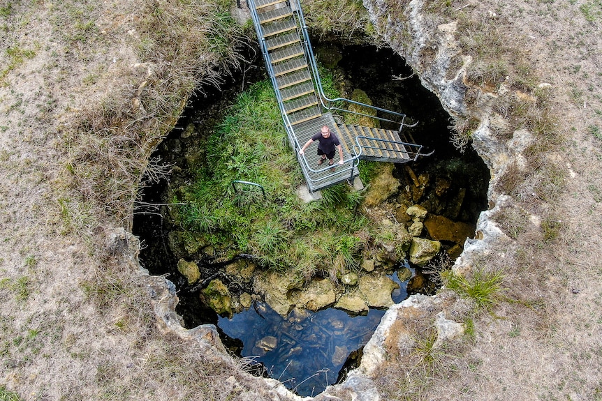 A drone photo of a man standing on a ladder descending into a submerged cave.