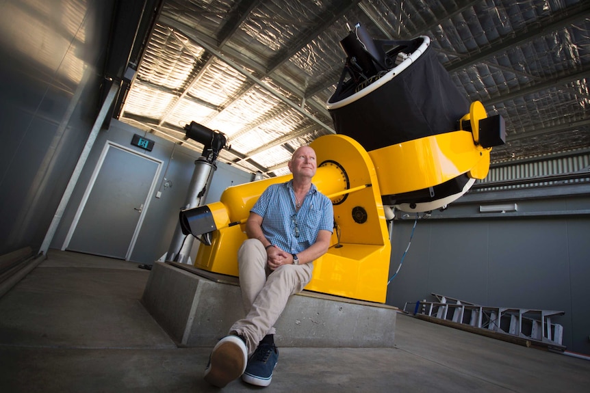 David Coward sits alongside the bright yellow and black Zadko telescope.