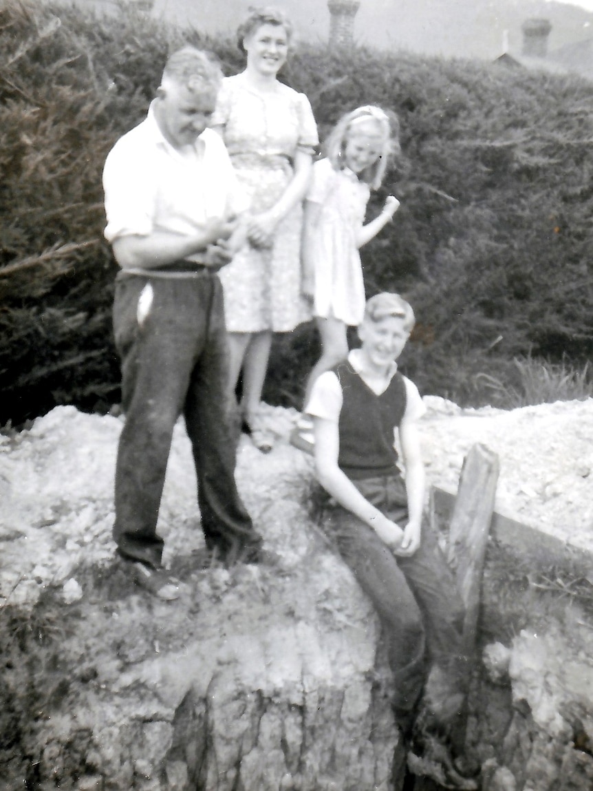 A black and white image of group of people at the edge of hole dug in a backyard in the 1940s