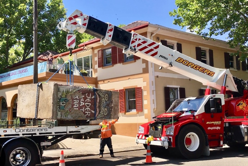 A graffiti slab of wall is being moved by a crane