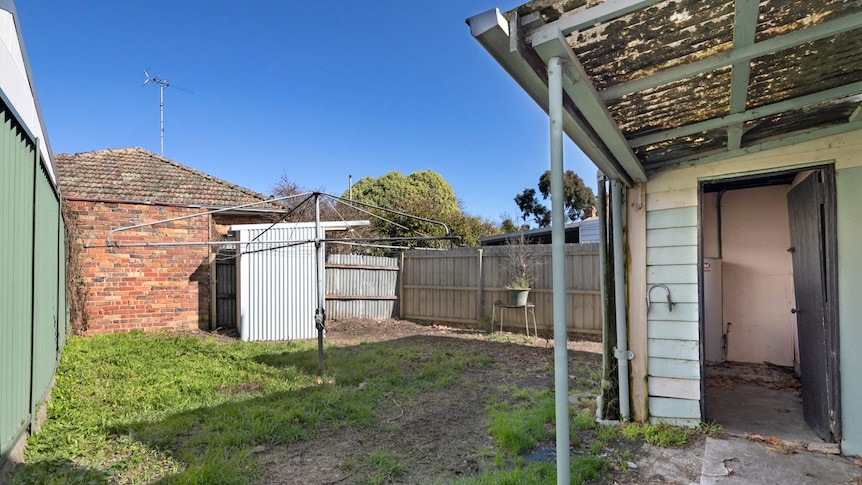 A backyard with patchy grass, a clothes line and a corrugated iron structure at the back. 