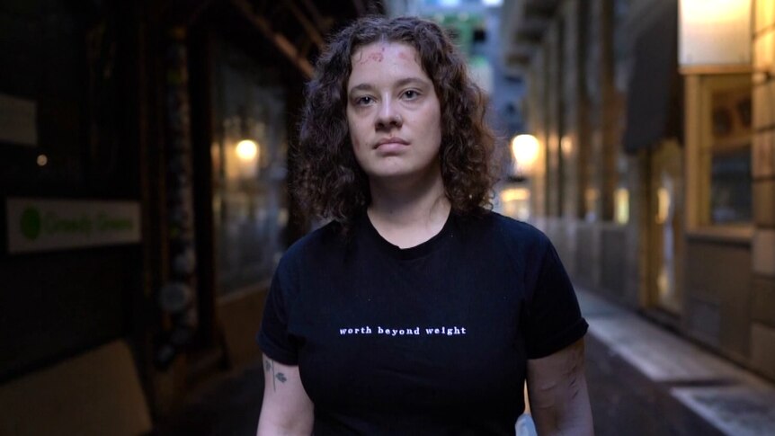 Person standing in a Melbourne laneway, wearing a black shirt that says 'worth beyond weight'.