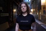 Person standing in a Melbourne laneway, wearing a black shirt that says 'worth beyond weight'.
