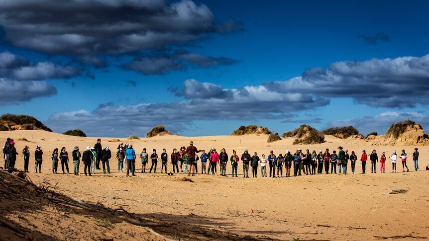 Students gather in a line on the plains of Lake Mungo, listening to a man talk.