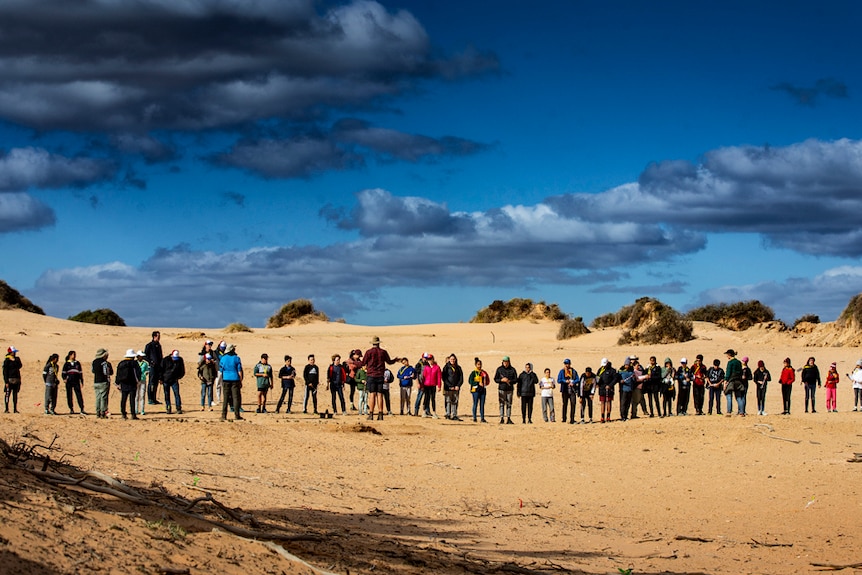 Students gather in a line on the plains of Lake Mungo, listening to a man talk.