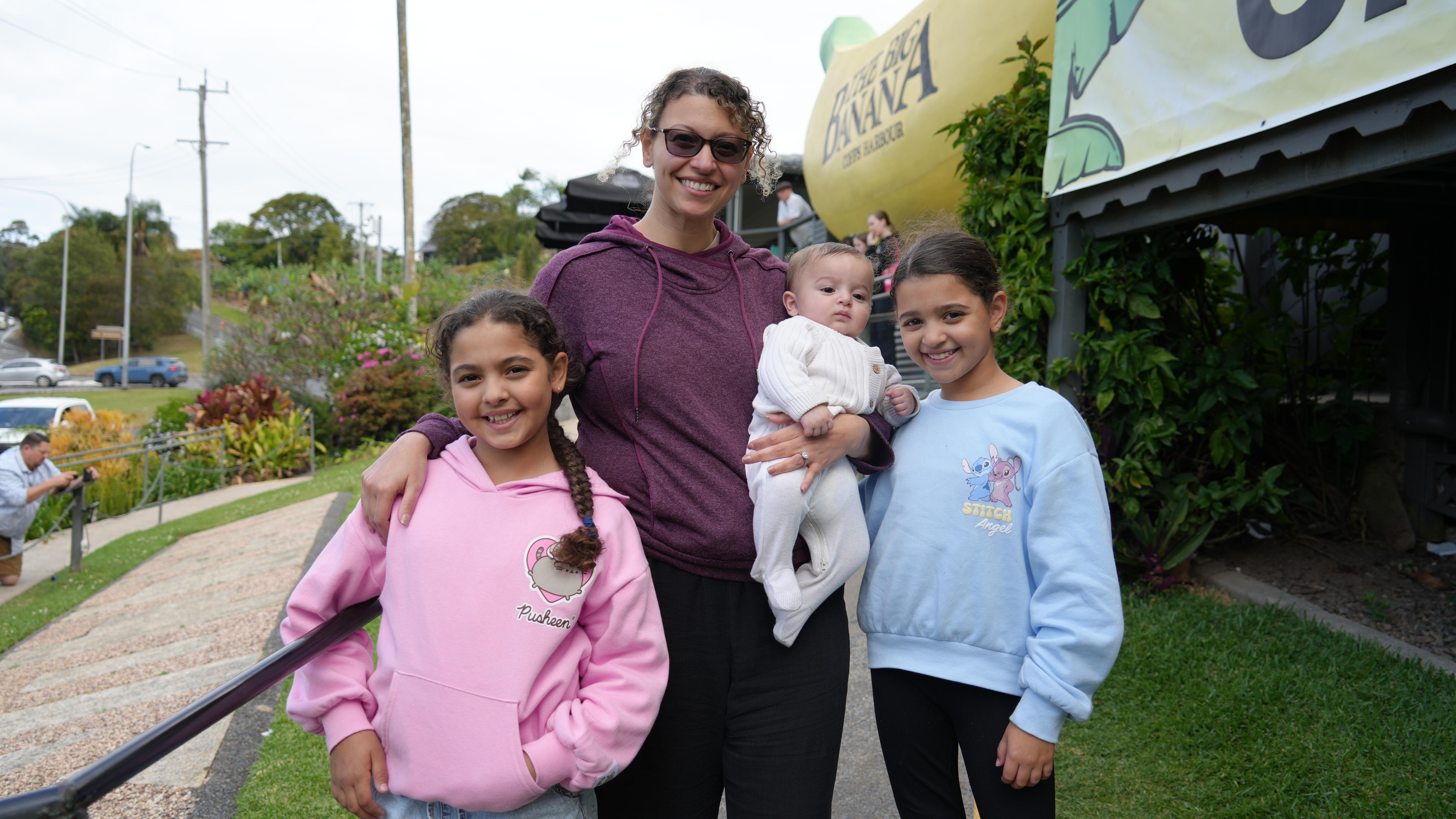 A smiling woman stands with her three young children in front of the Big Banana.