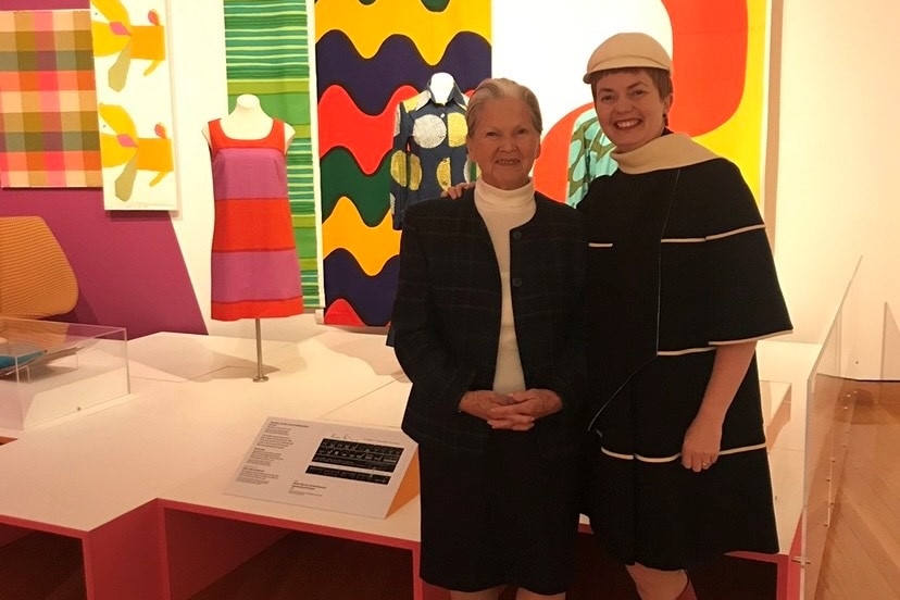 Charlotte dressed in all black with her daughter rebecca also dressed in all black standing against a colour art gallery wall.