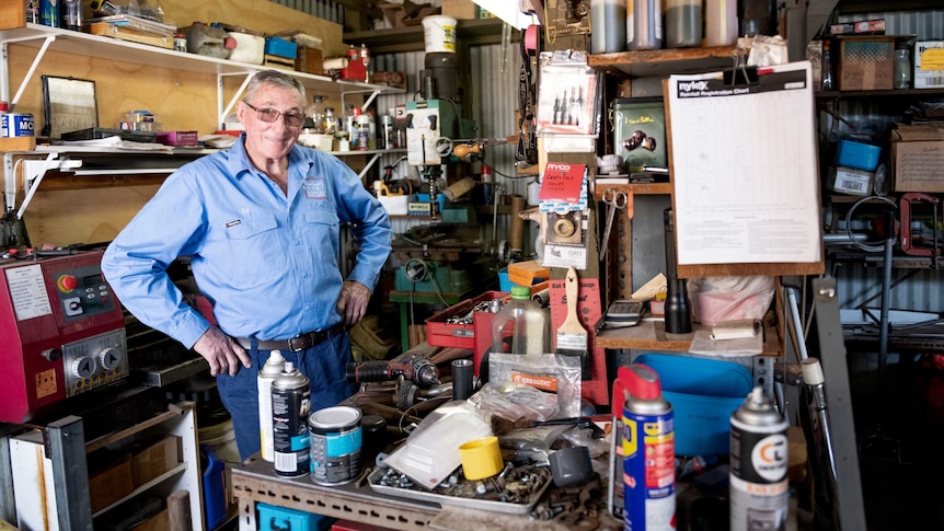 Mid shot of older man standing with hands on hips at work bench in a shed