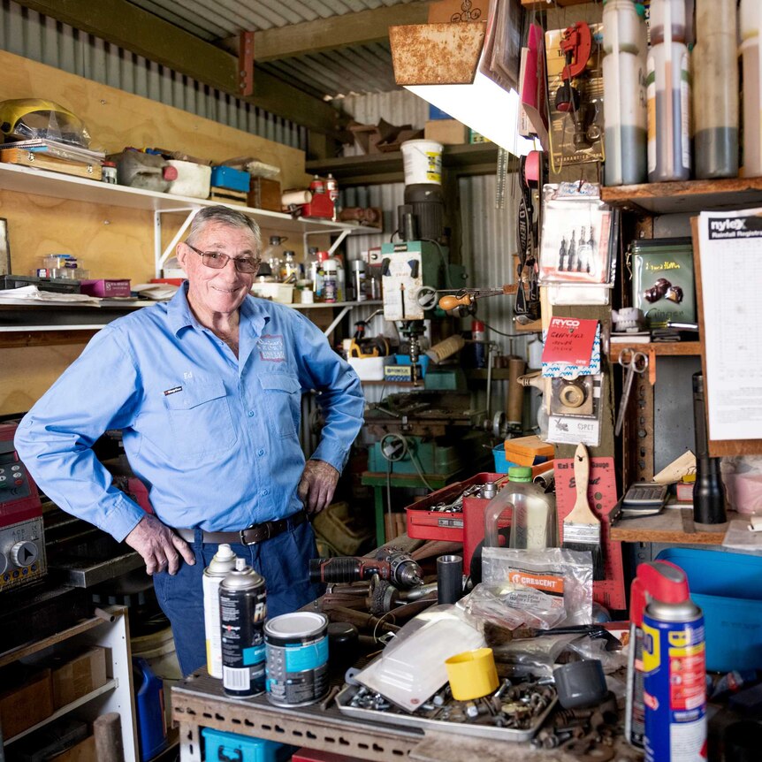 Mid shot of older man standing with hands on hips at work bench in a shed